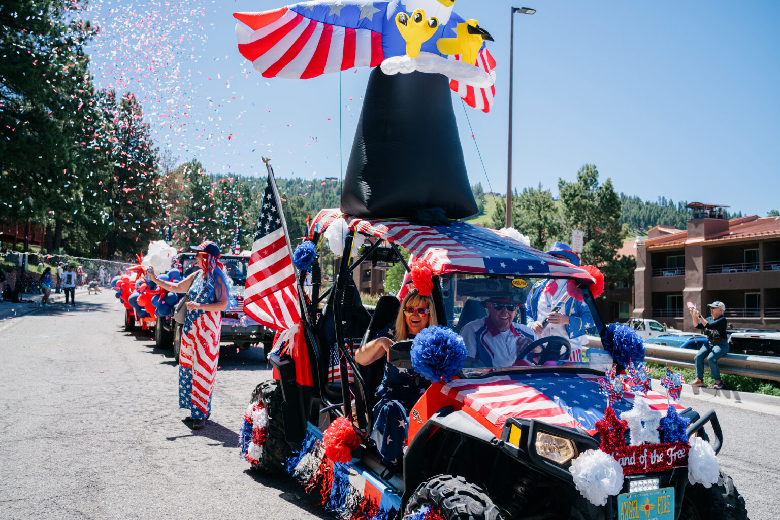 Patriotic parade float covered in American flags and red, white, and blue decorations with confetti in the air.
